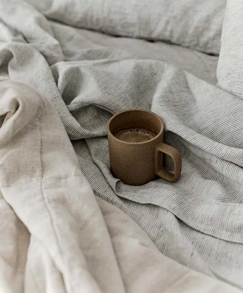 A ceramic coffee mug resting on textured natural linen bedding
