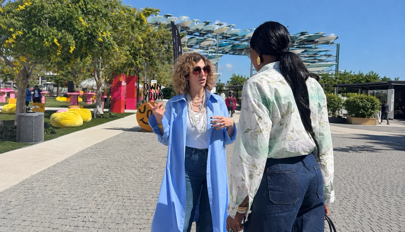 Vivianka Lavin in a long blue shirt dress talking with Yaima Ortiz on a sunny promenade