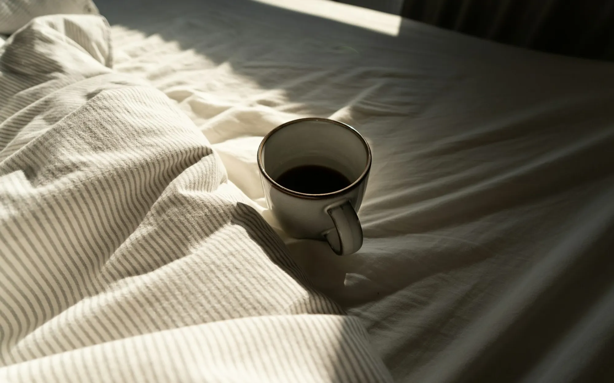 A cup of coffee resting on rumpled cream bedding