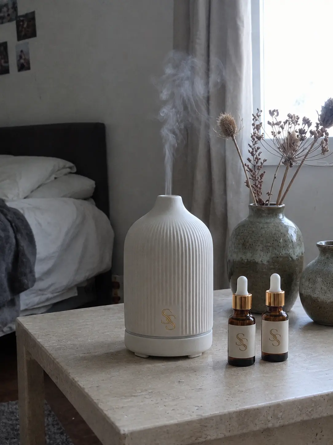 The ribbed ivory Spry diffuser misting beside two amber essential-oil bottles