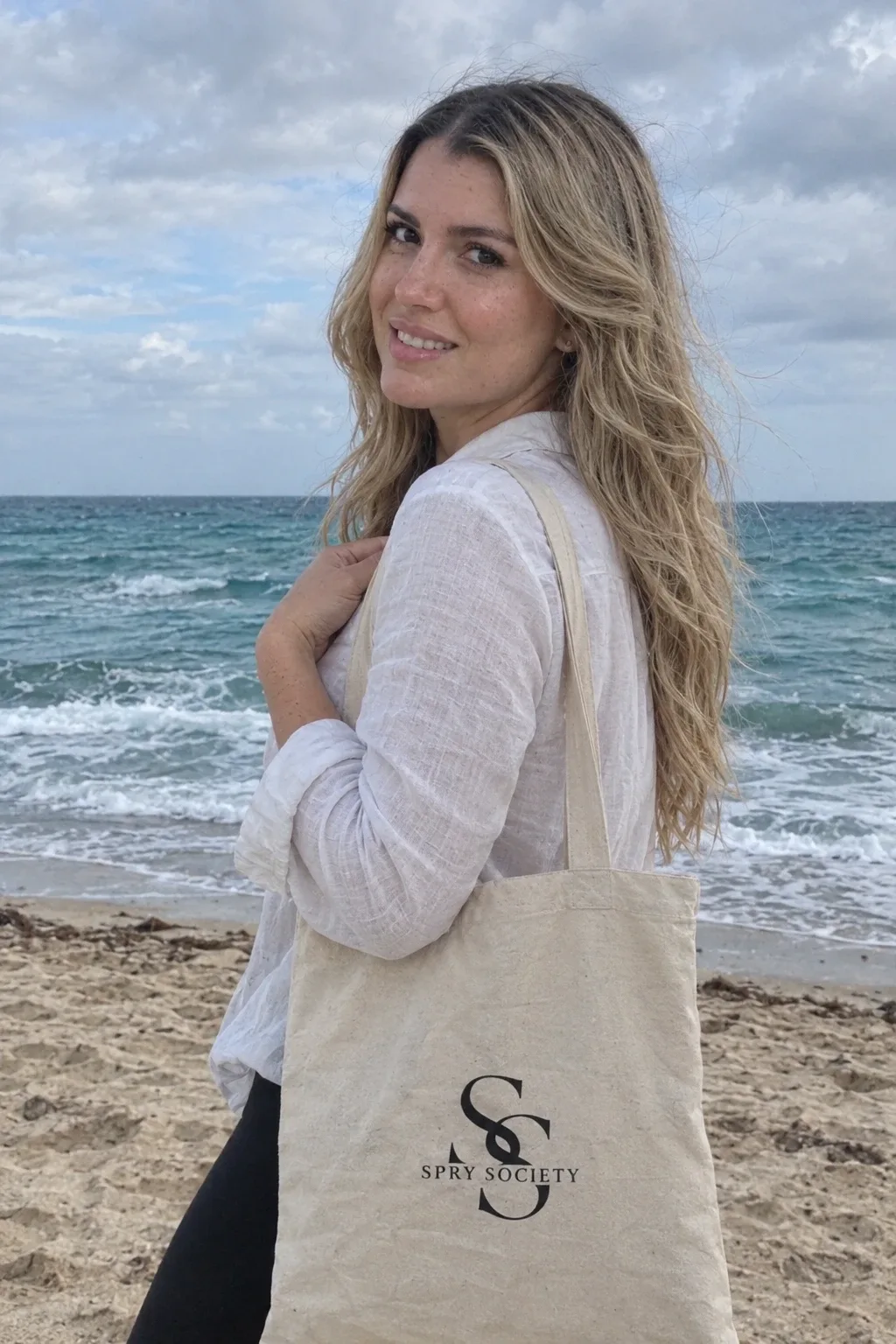 Maria Olivera on the beach with the canvas Spry Society tote bag over her shoulder